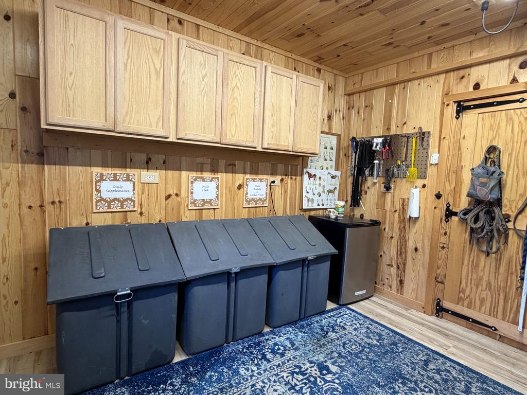 Wood-paneled storage room with overhead cabinets, labeled bins, a small refrigerator, and mounted tools.