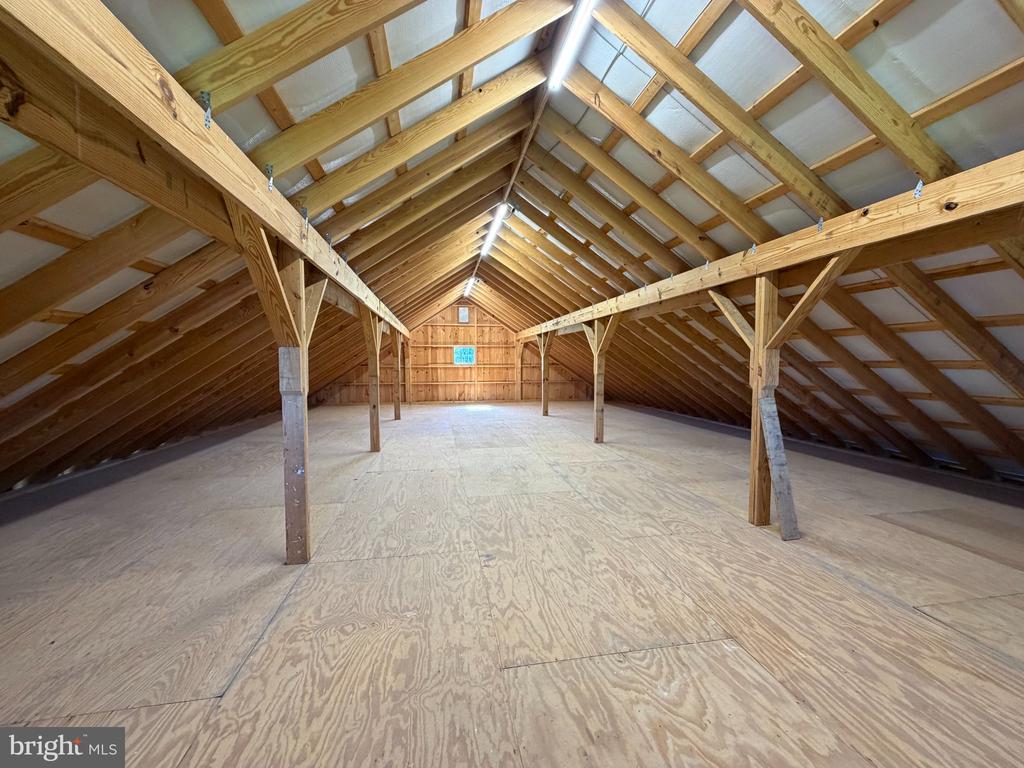 Unfinished attic with a plywood floor and exposed wooden roof trusses.