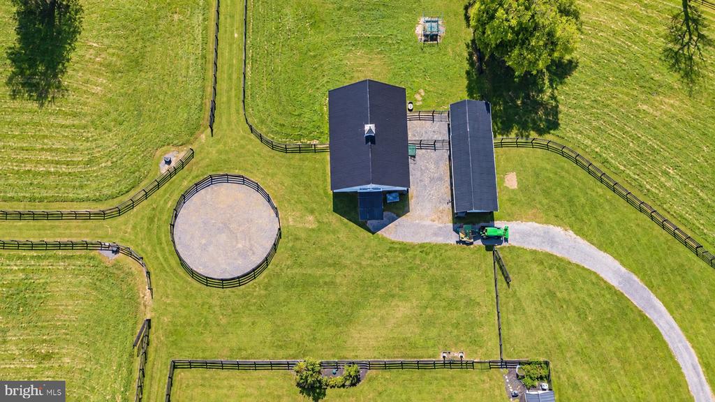 Aerial view of two farm buildings, fenced pasture, and a circular riding pen.