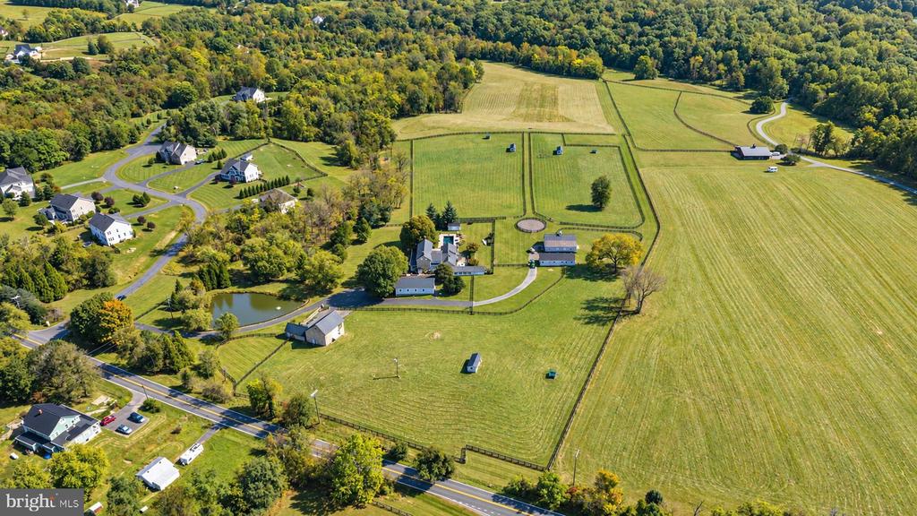 Aerial view of broad fields, farm buildings, a pond, and neighboring homes.