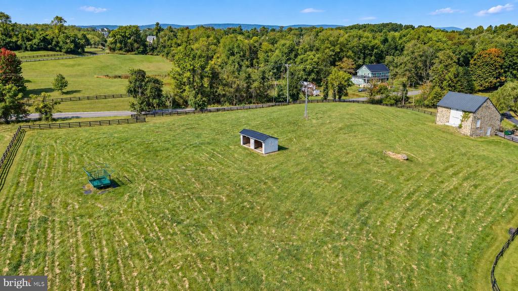 Aerial view of a fenced pasture with a small shed and stone outbuilding.