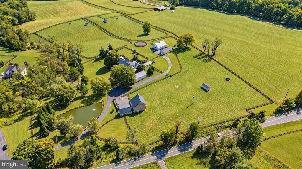 Aerial view of fenced pastures, multiple buildings, and a pond at a rural property.