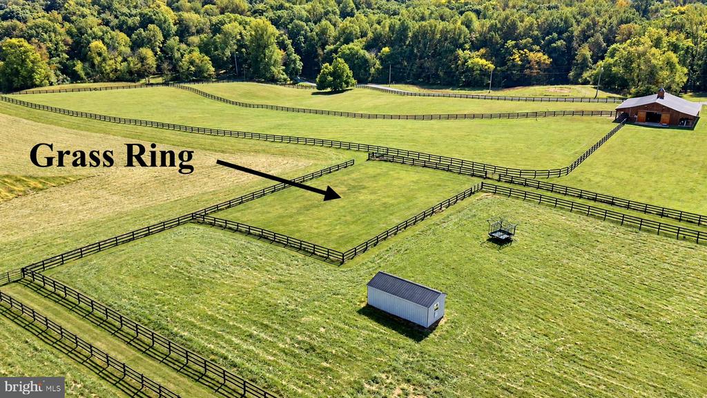 Aerial view of fenced pastures with a marked grass ring, barn, and small shed.