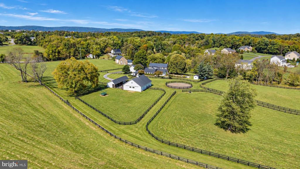 Aerial view of a fenced rural property with barns, paddocks, and a circular riding arena.