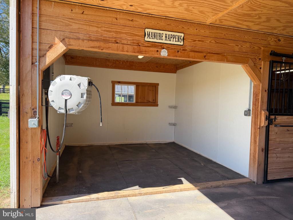 Wooden barn bay with a wall-mounted hose reel, small window, and “MANURE HAPPENS” sign.