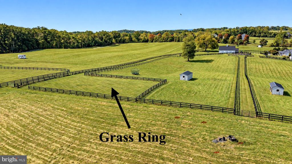 Aerial view of fenced green pasture with a circular grass ring and small sheds.