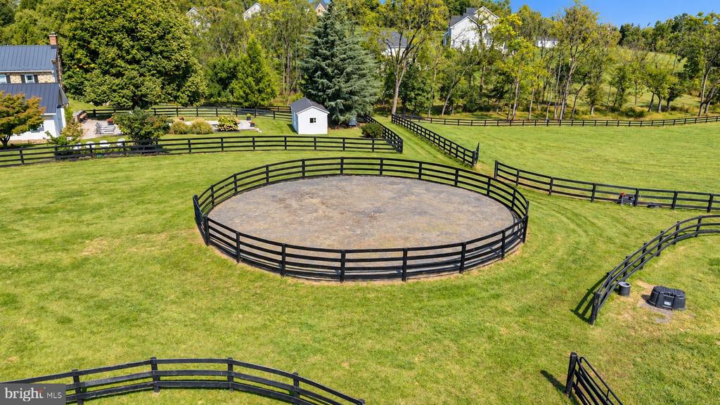Aerial view of a fenced circular riding arena surrounded by green paddocks and trees.