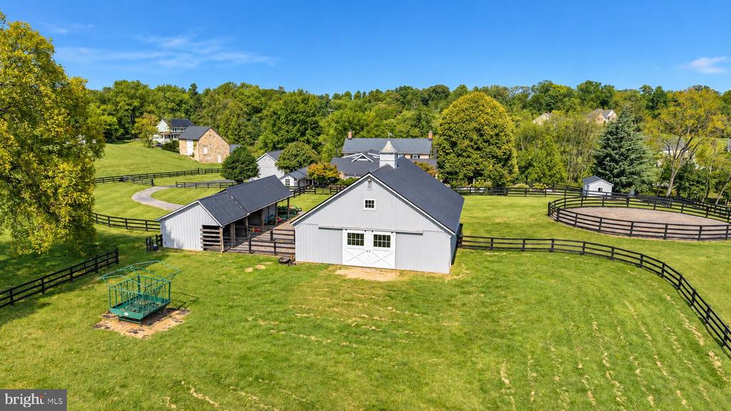 Aerial view of a property with white barns, fenced green paddocks, and wooded surroundings.