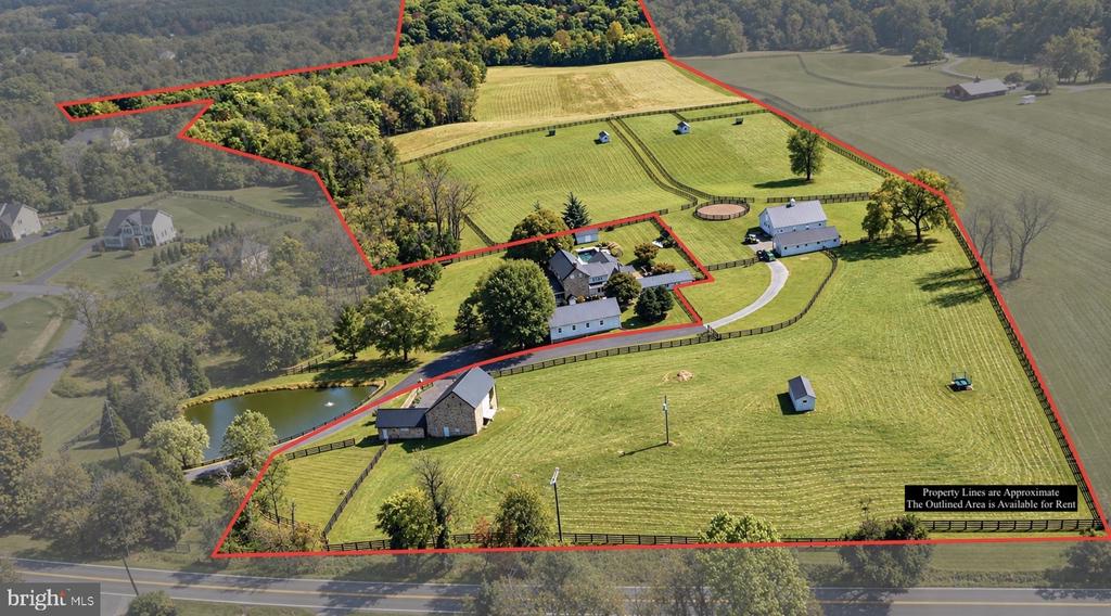 Aerial view of outlined rural acreage with fenced fields, several buildings, and a pond.