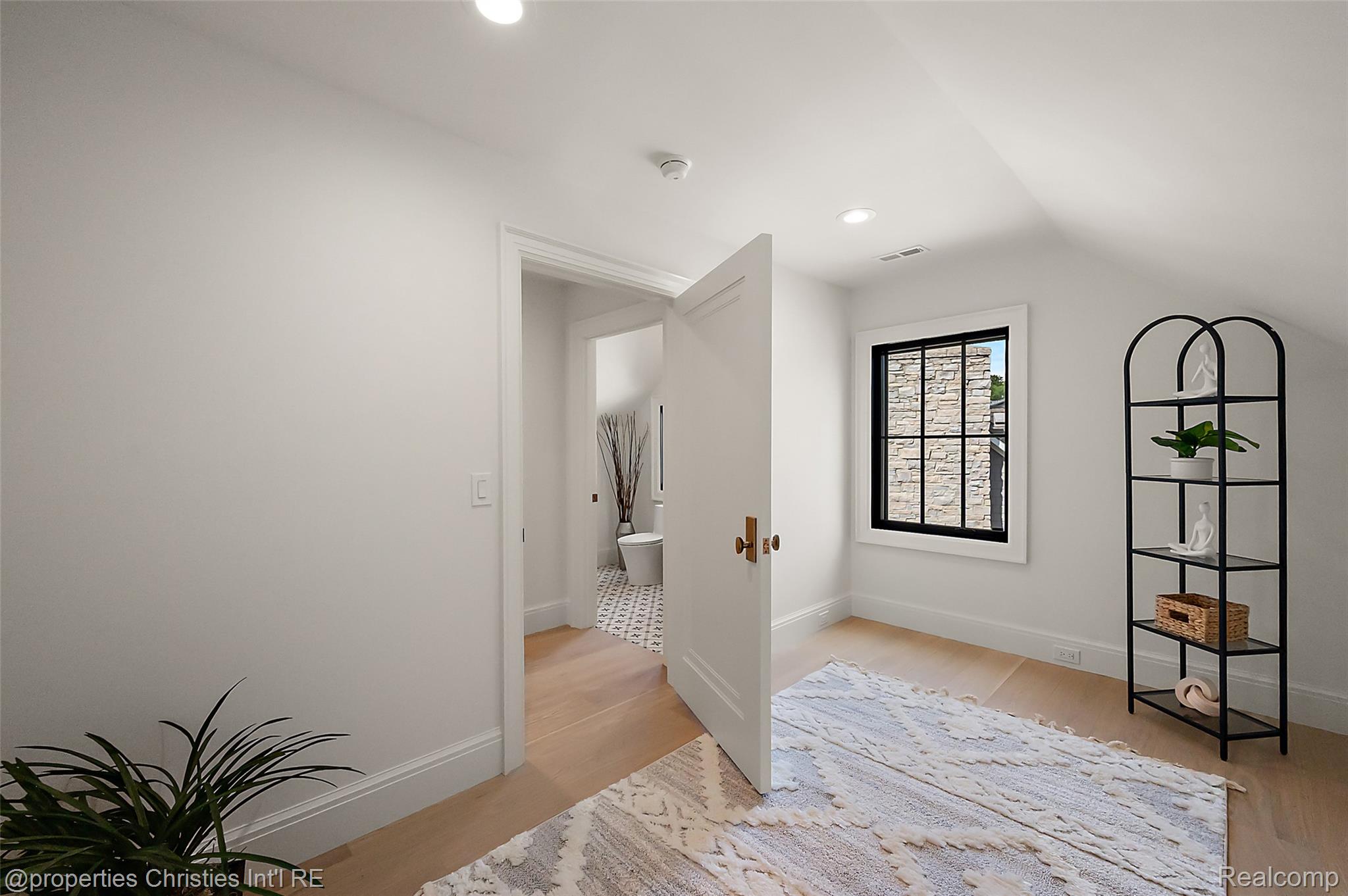 Bright staged room with a black-framed window, arched display shelf, and open door to a tiled bathroom.