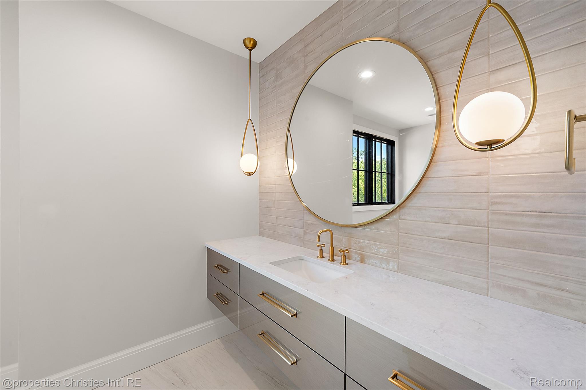 Bathroom vanity with a round brass-framed mirror, pale tile, and brass fixtures.