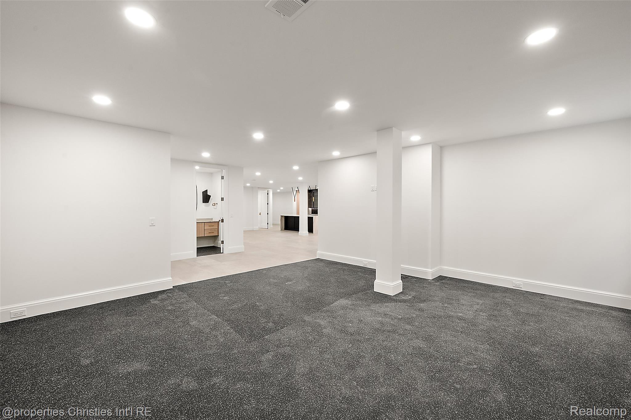 Finished basement with dark carpet, recessed lights, and a support column.