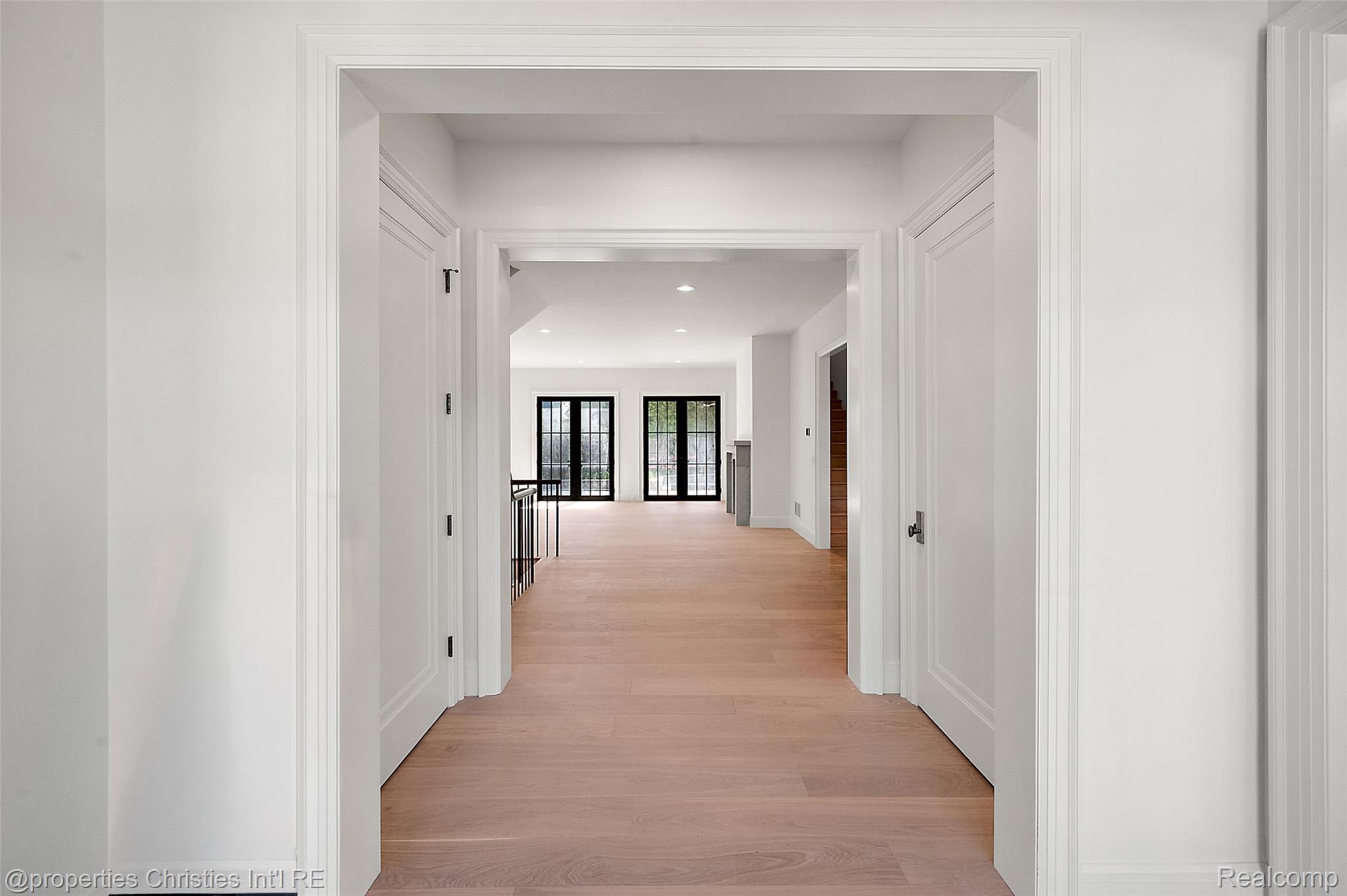 Vacant hallway with light wood floors, white paneled trim, and black-framed glass doors at the far end.