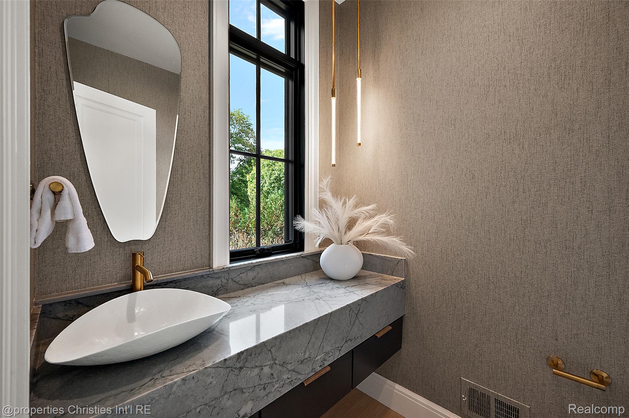 Bathroom vanity with a white vessel sink, gray marble counter, brass faucet, and black-framed window.