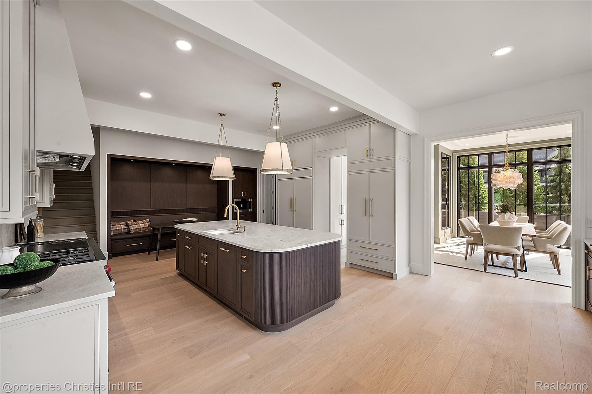 Kitchen with a dark wood island and built-in cabinetry, opening to a bright dining area with tall windows.