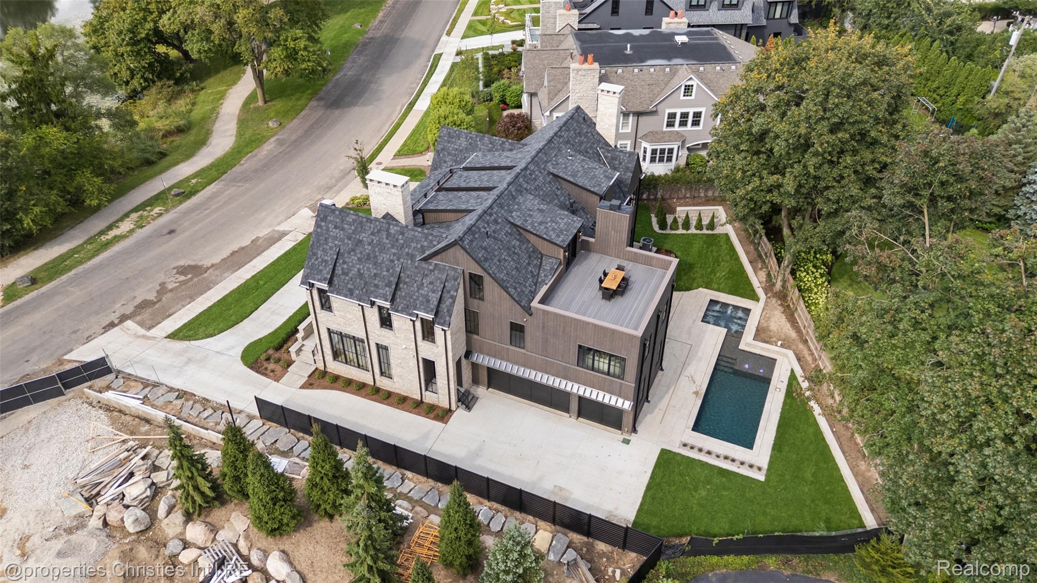 Aerial view of a modern stone-and-wood home with a raised deck and long swimming pool.