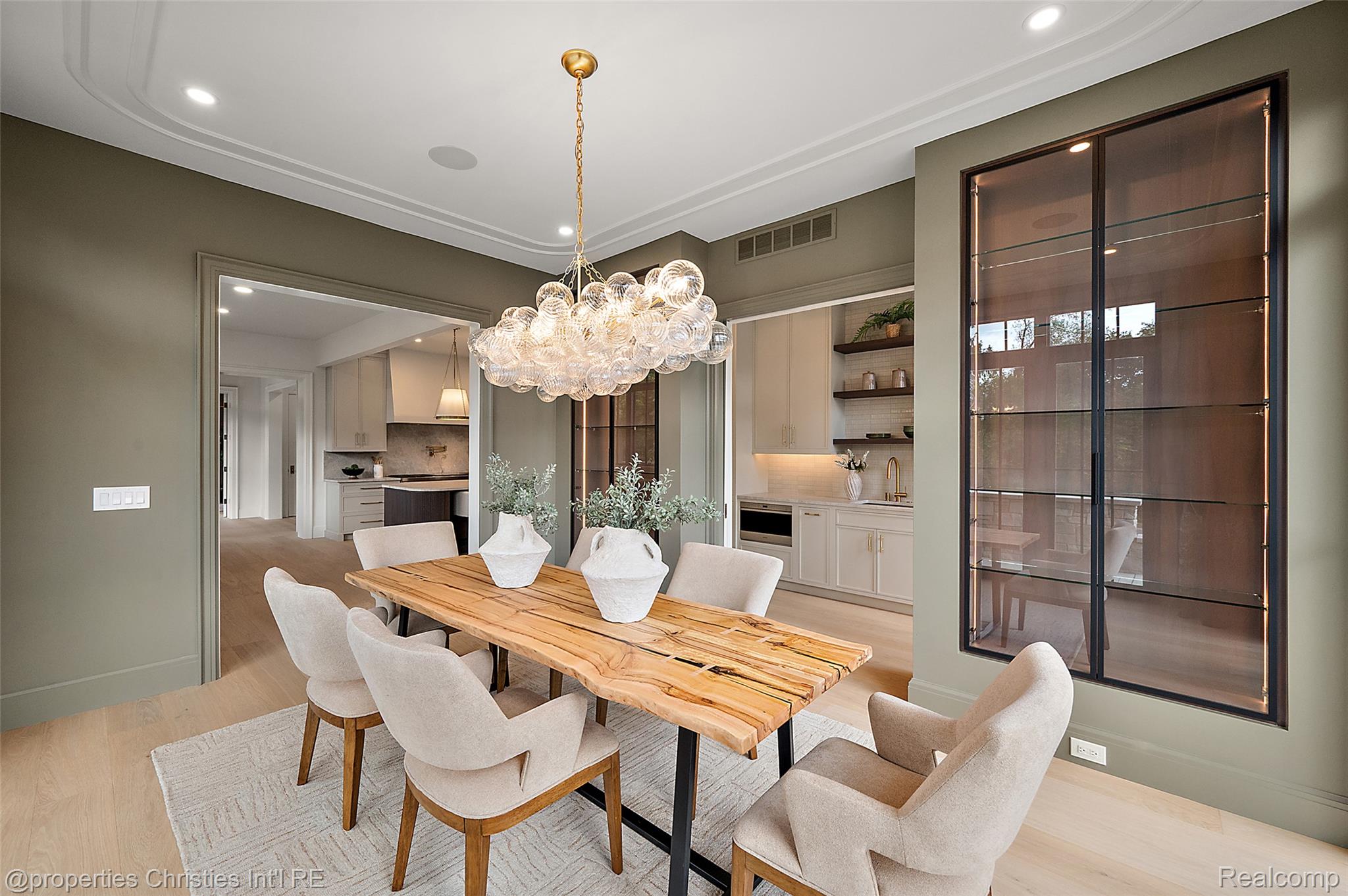 Dining room with a long wood table, sculptural glass chandelier, and tall shaded windows.