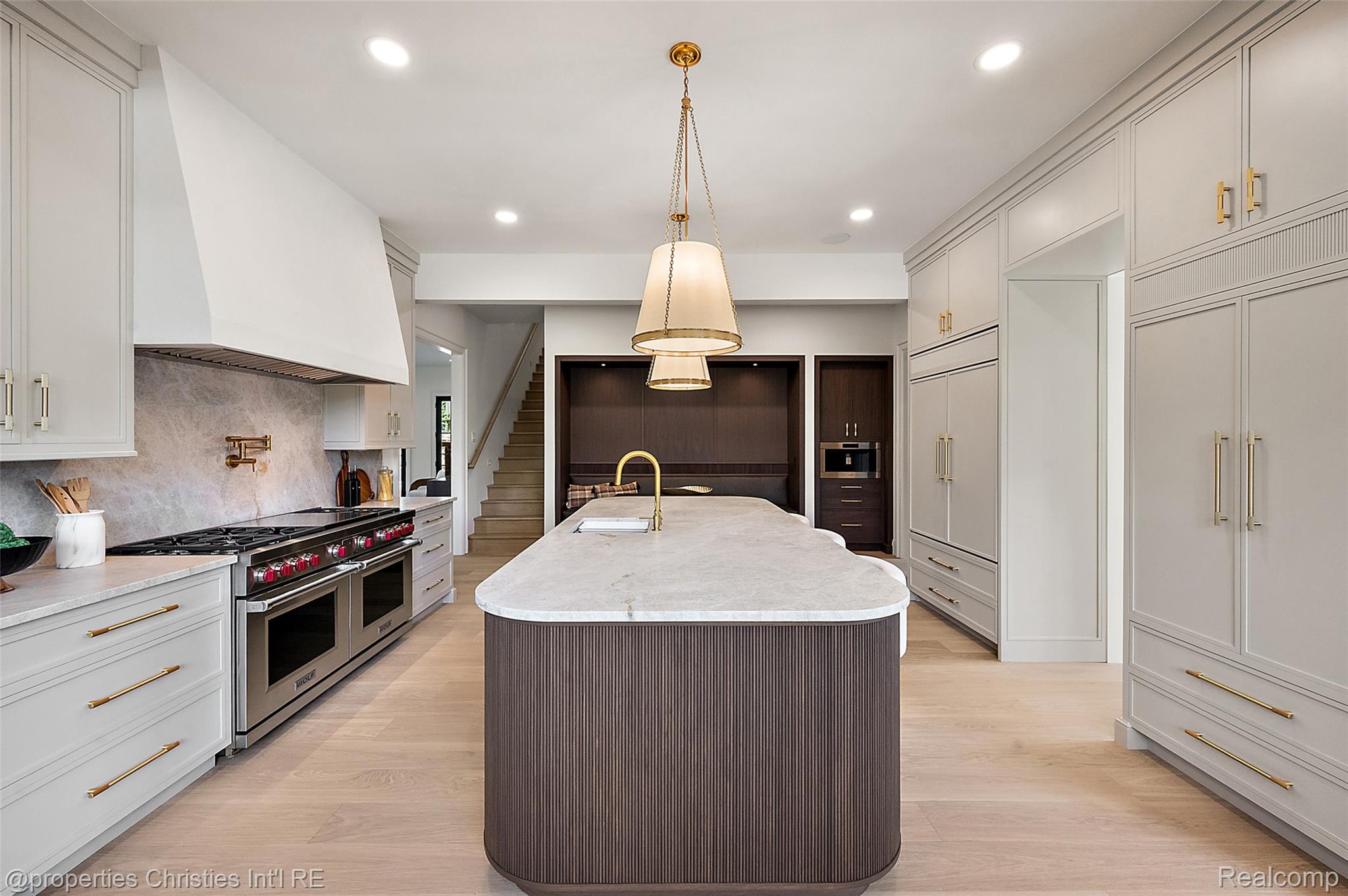Kitchen with a large rounded island, brass fixtures, paneled cabinetry, and a professional gas range.