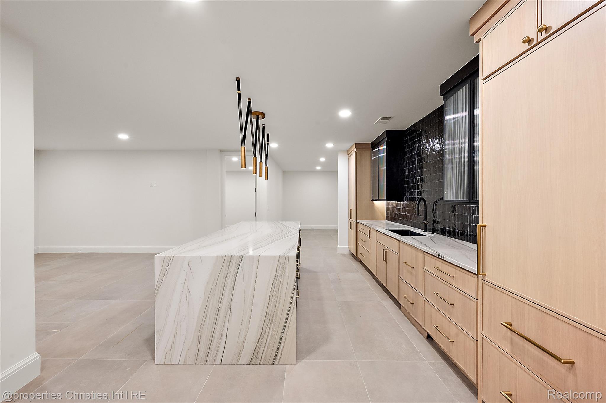 Modern kitchen with a veined marble island, pale wood cabinets, and a glossy black tile backsplash.