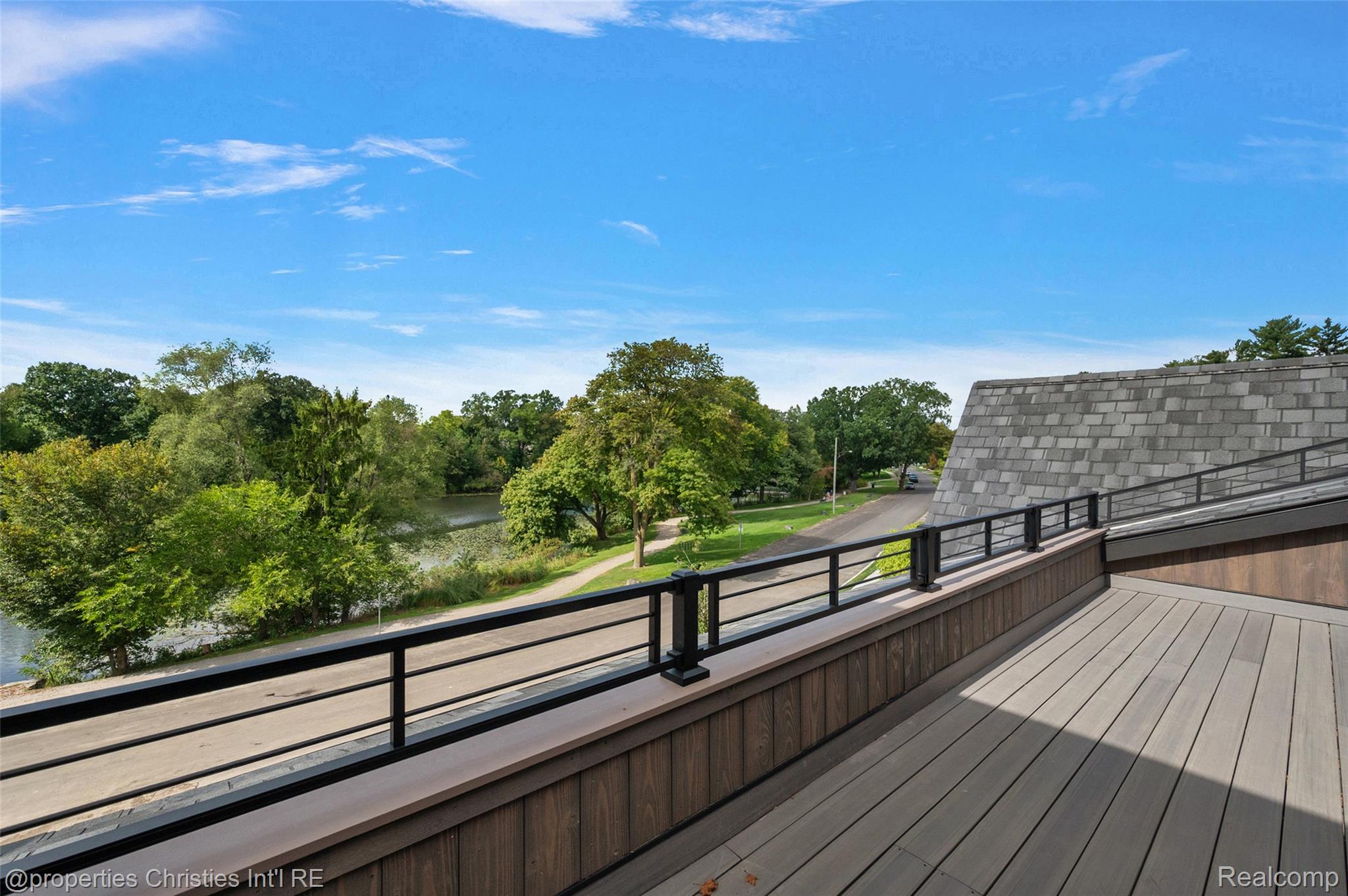 Rooftop deck overlooking a tree-lined lake and walking path.
