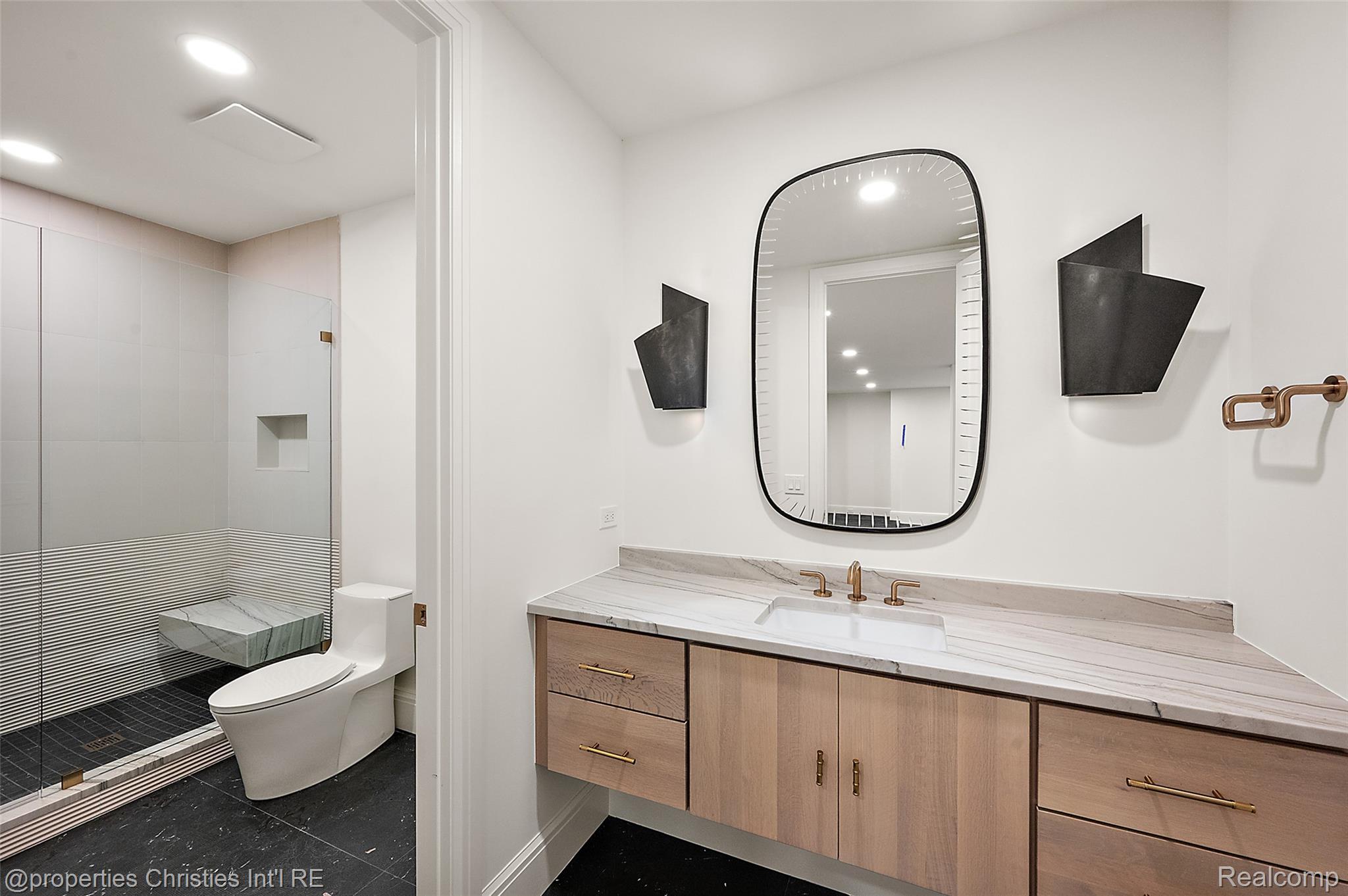 Contemporary bathroom with a floating wood vanity, rounded mirror, and glass-enclosed tiled shower.