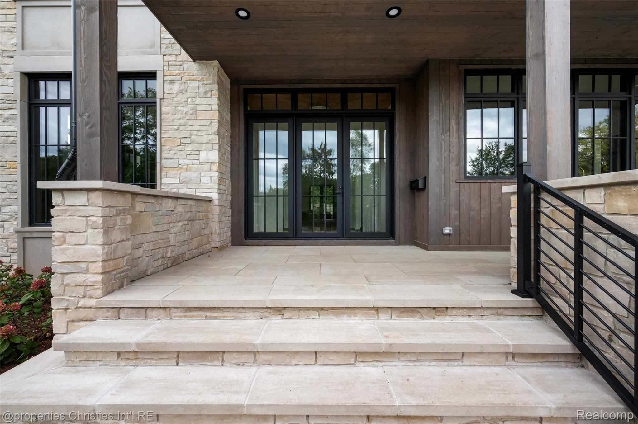 Covered stone front entry with broad steps, black-framed glass doors, and a dark metal railing.