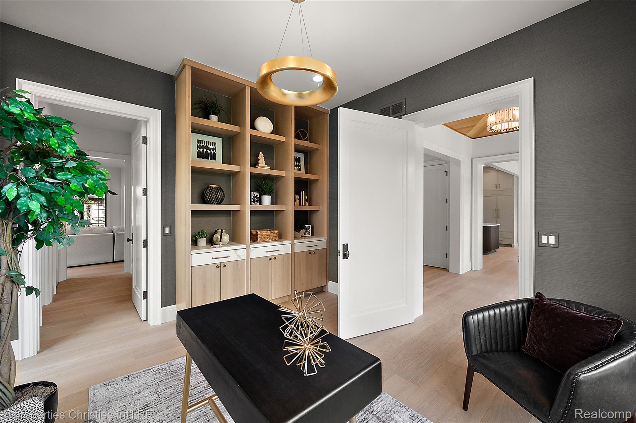 Home office with light wood built-in shelves, a black desk, and a leather chair.