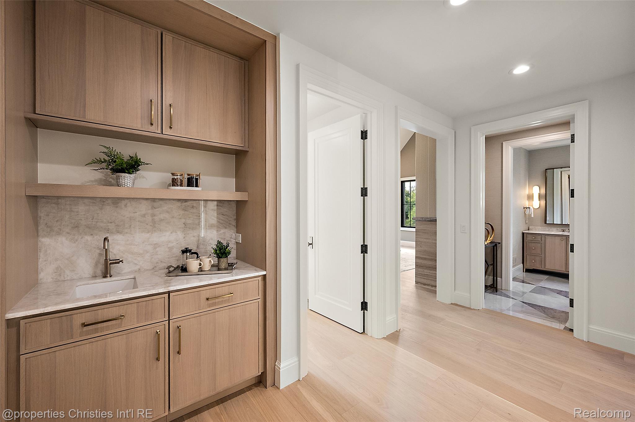 Built-in wood wet bar with sink and stone backsplash beside open doorways to a bedroom and bathroom.