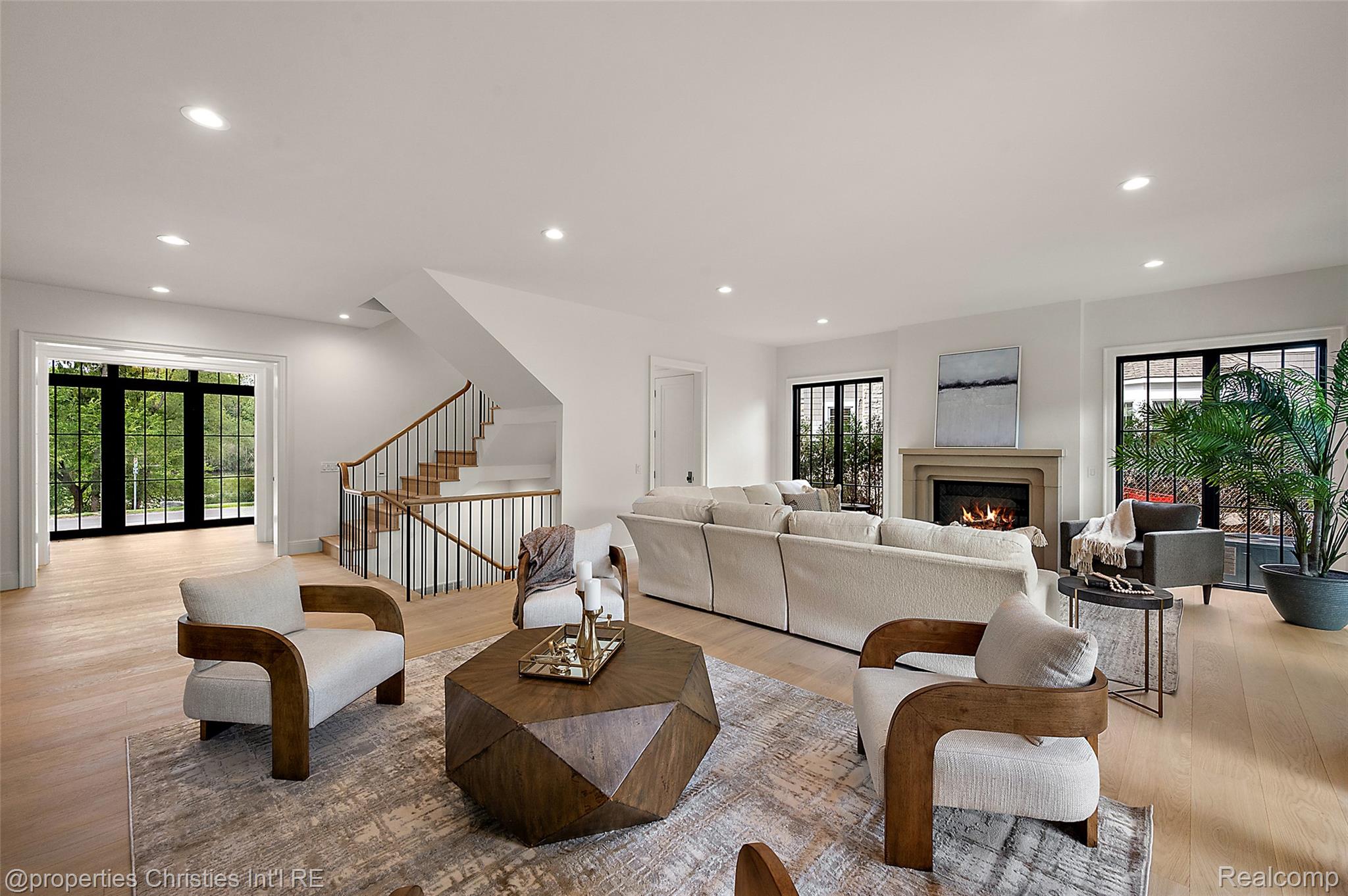 Staged living room with a fireplace, staircase, and black-framed windows.