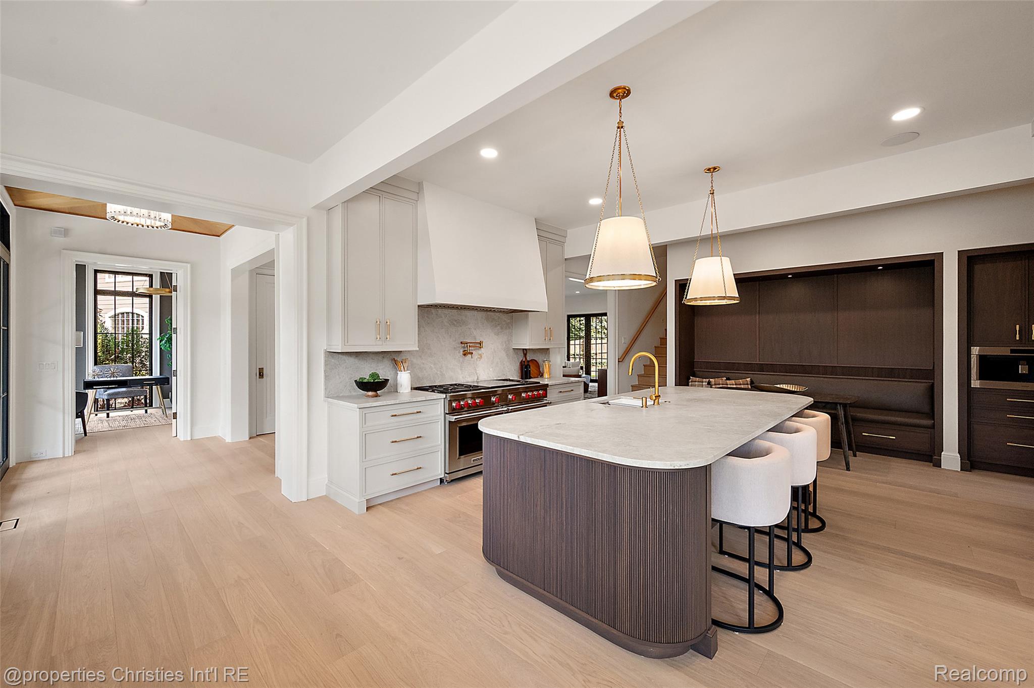 Modern kitchen with a large curved island, brass fixtures, white cabinetry, and a dark built-in banquette.