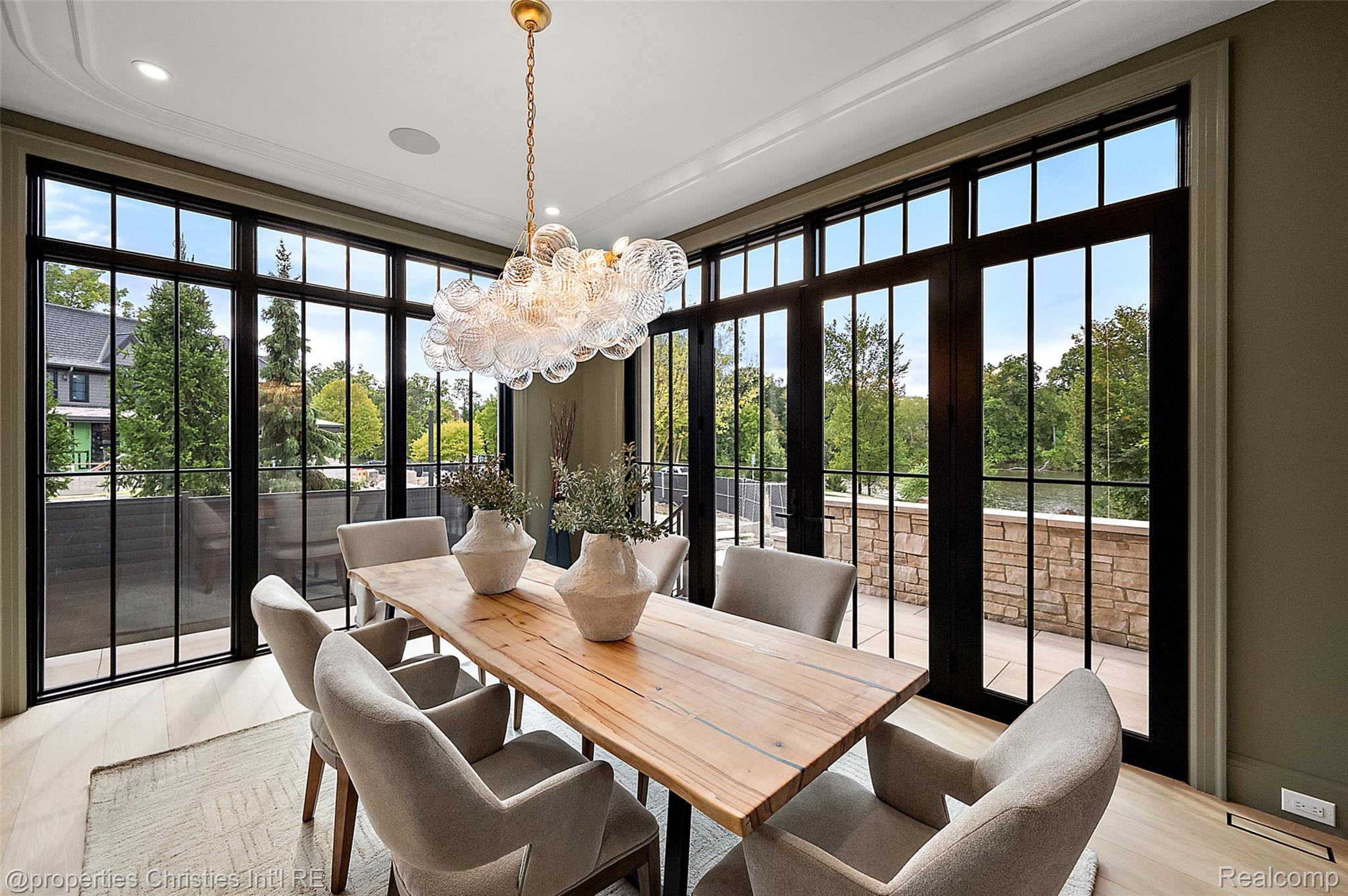 Dining room with a long wood table, glass chandelier, and expansive black-framed windows opening to a terrace.