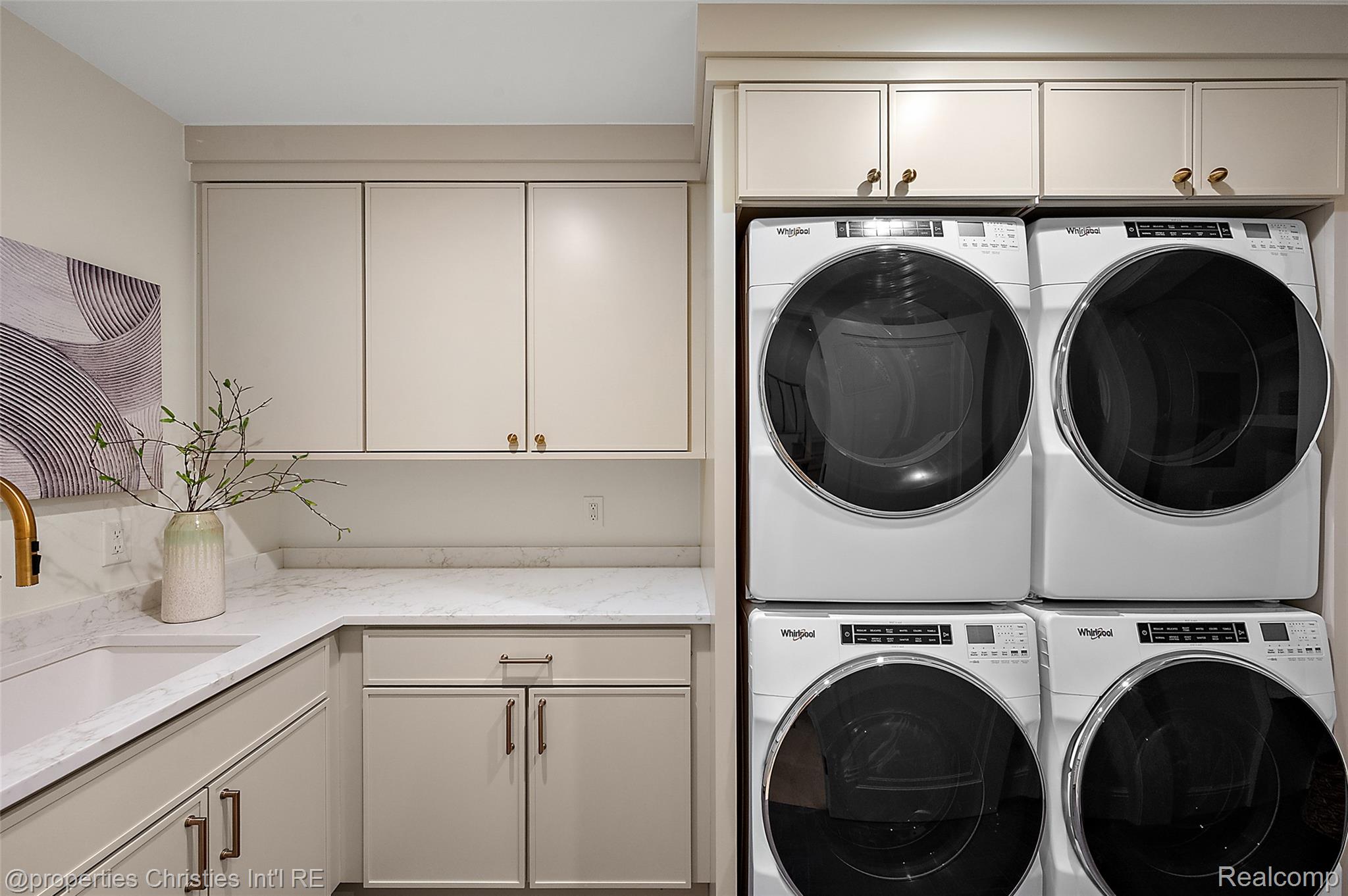 Laundry room with stacked Whirlpool washer-dryer pairs, cream cabinets, and a marble-look counter.