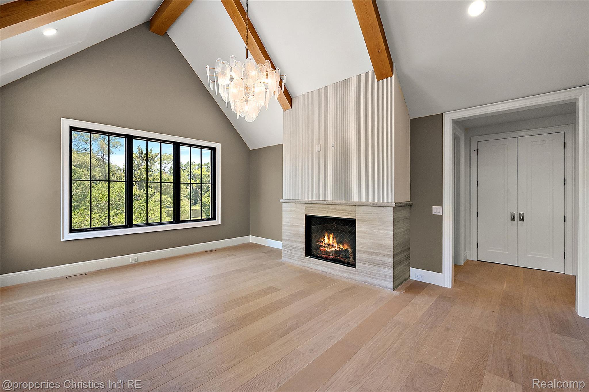 Living room with vaulted wood-beam ceiling, large garden-view window, and lit fireplace.