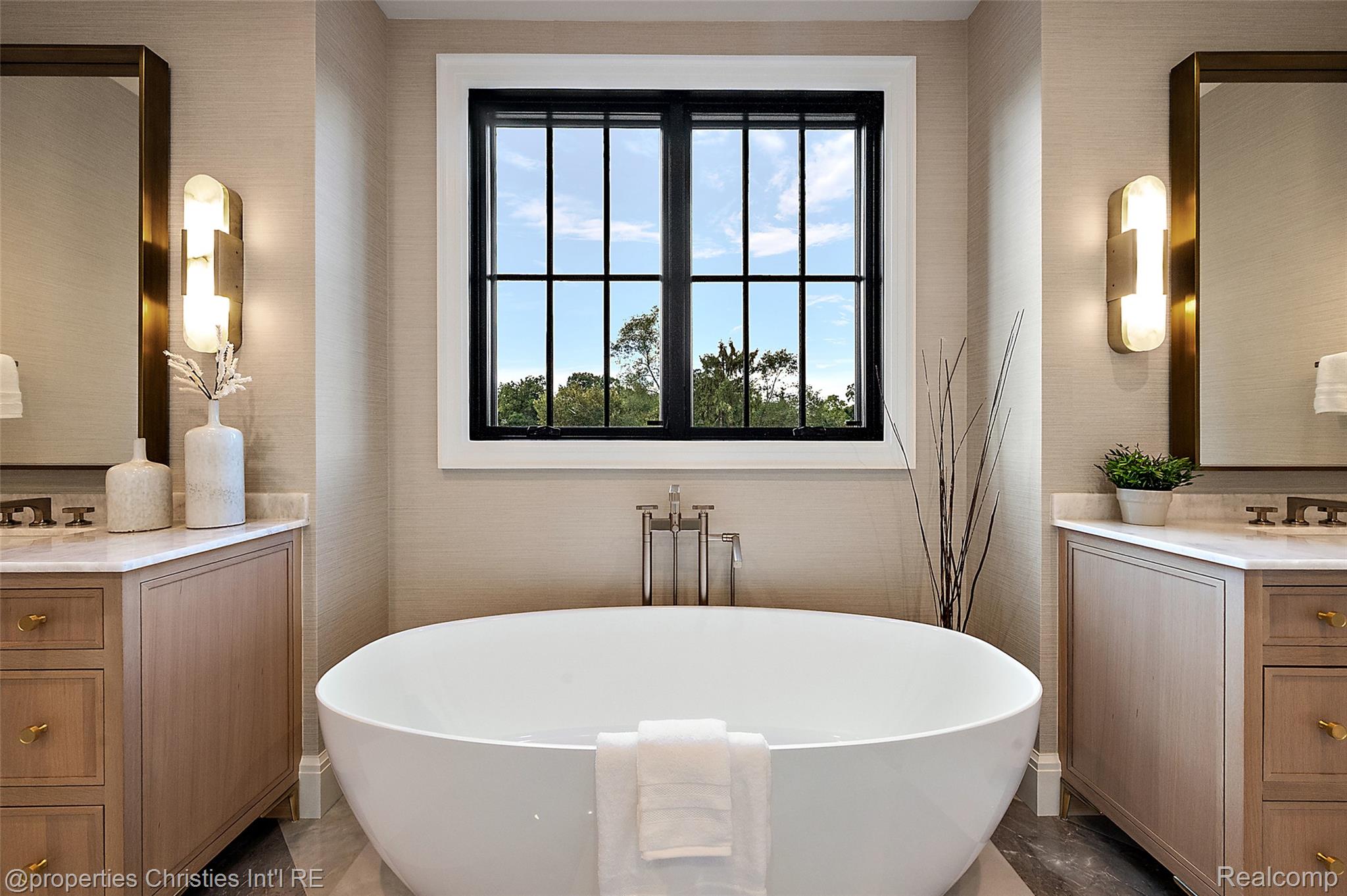 Bathroom with a freestanding soaking tub beneath a black-framed window, flanked by matching wood vanities.