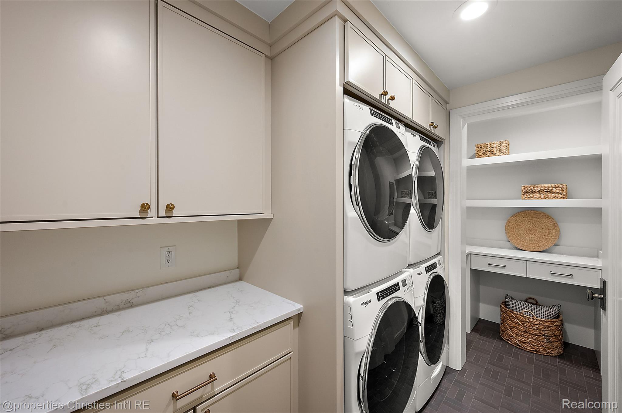 Laundry room with stacked front-loading machines, cream cabinets, and built-in shelving with woven baskets.
