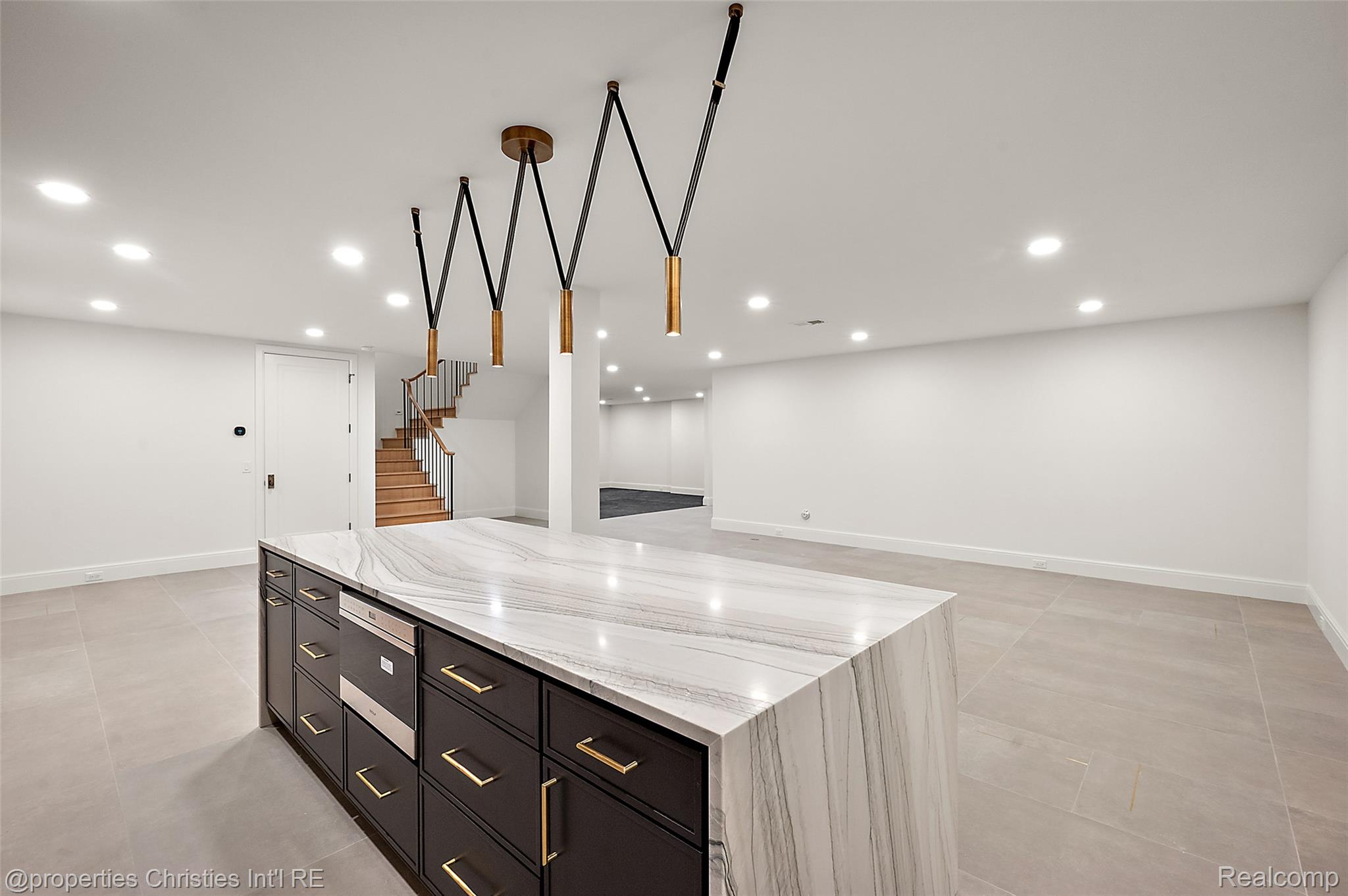 Finished kitchen with a veined stone island, dark cabinetry, brass hardware, and geometric pendant lights.