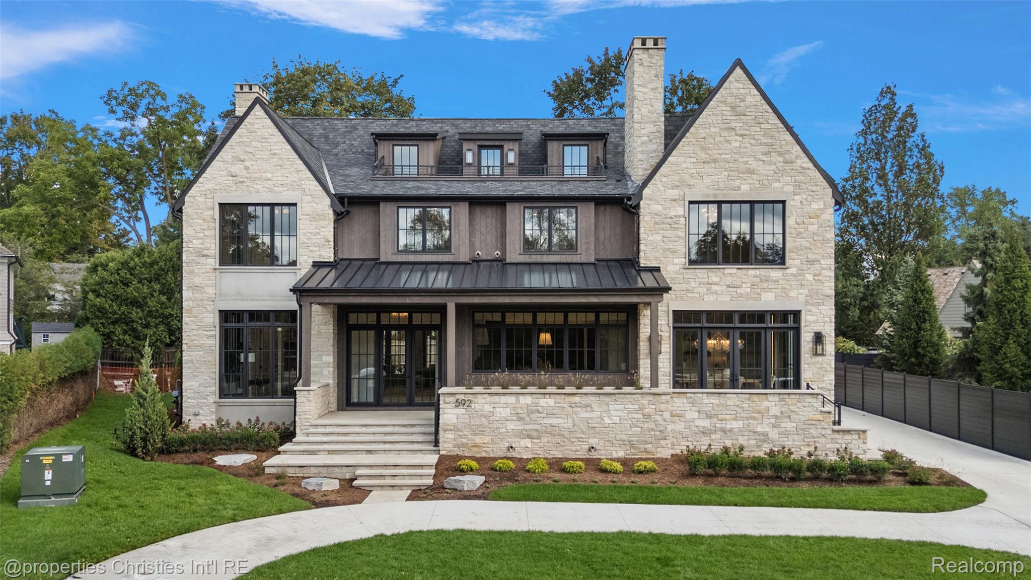 Stone-front house with steep gables, dark trim, and a landscaped lawn; number 592 appears on the terrace wall.