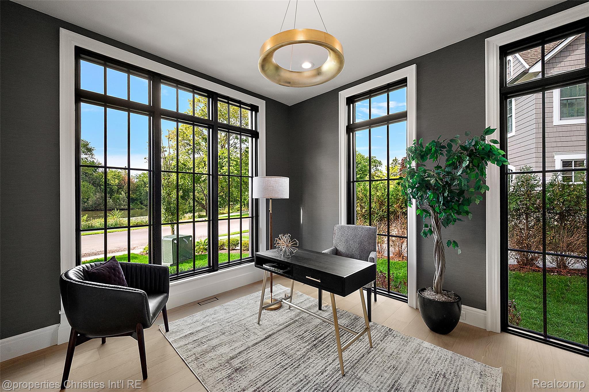 Staged home office with a black desk and chair beside expansive black-framed windows.