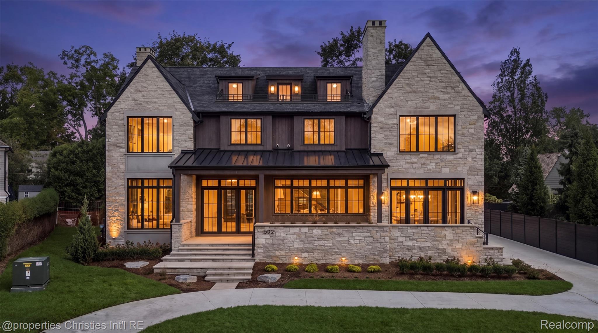 Stone house at dusk with steep gables, glowing windows, and a landscaped front lawn.
