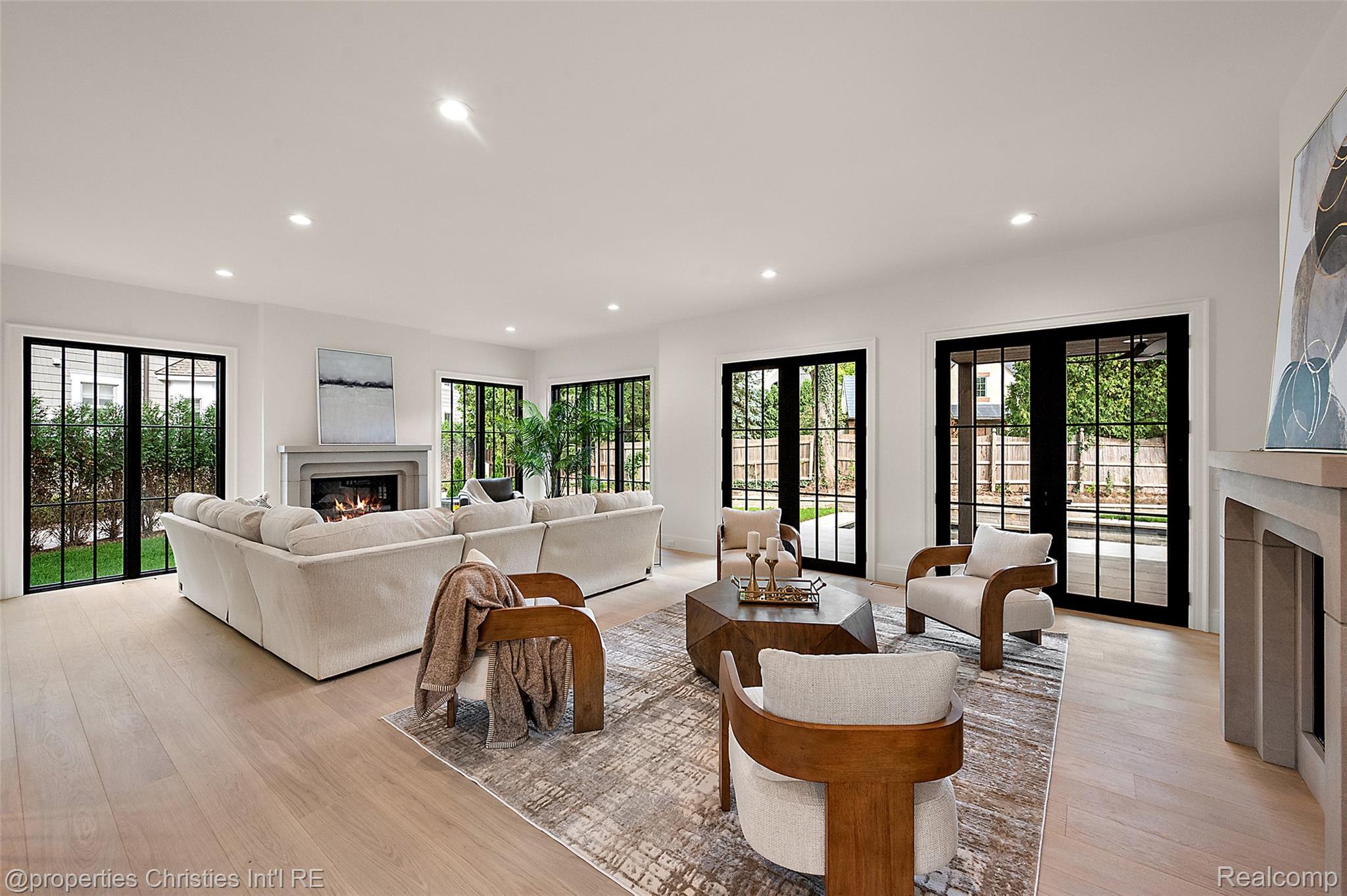Bright living room with a white sectional, two fireplaces, and black-framed doors to the yard.