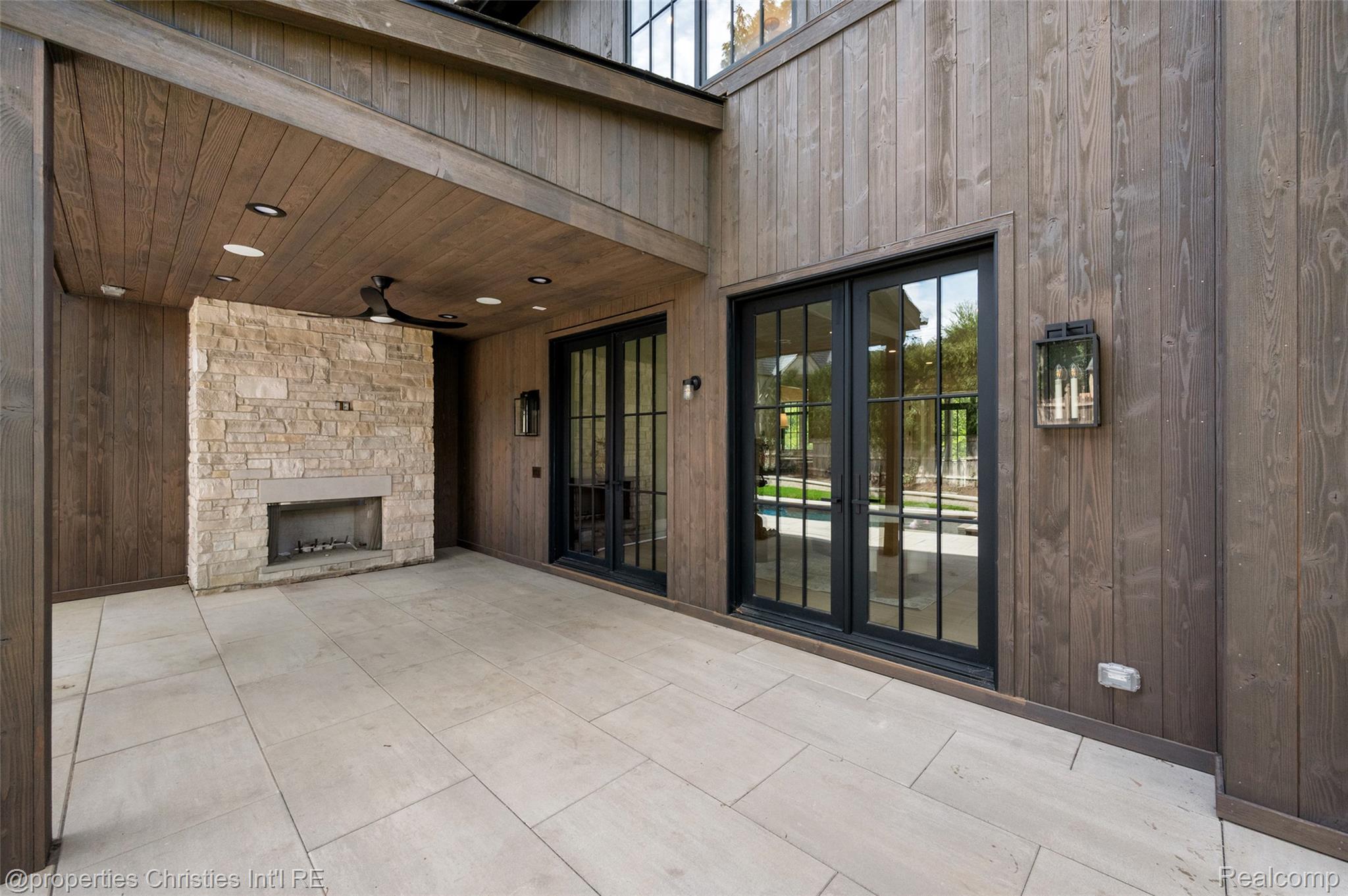 Covered patio with a stone fireplace and black-framed glass doors.