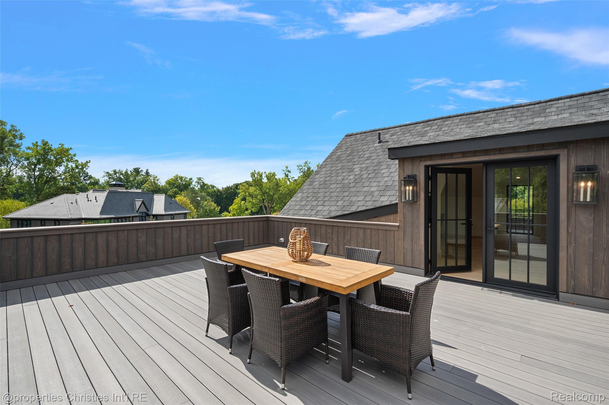 Furnished deck with a dining table and woven chairs beside black-framed sliding glass doors.