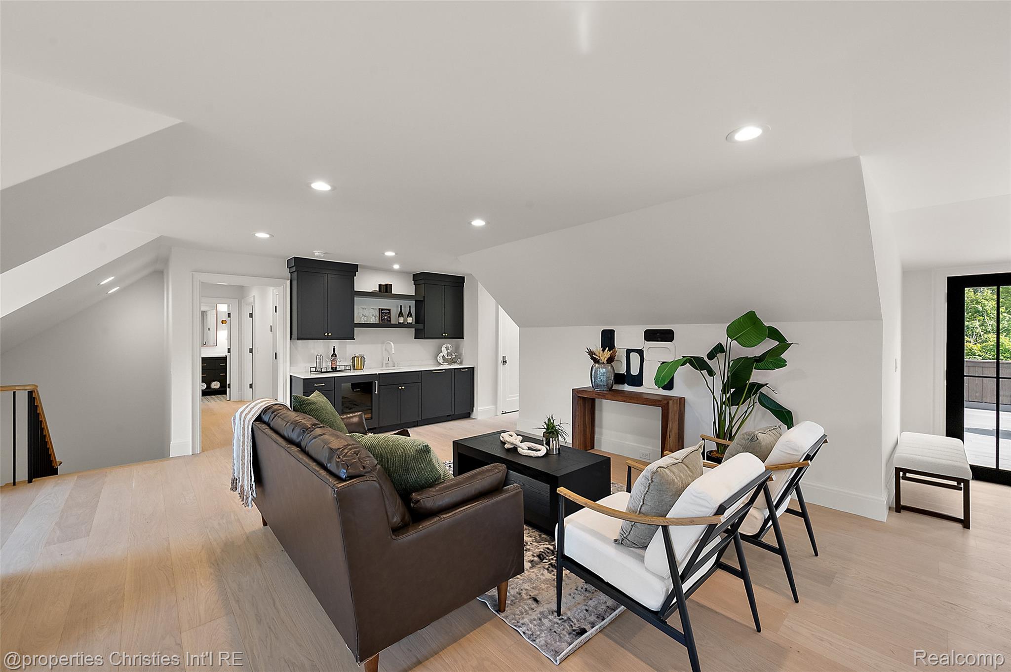 Attic lounge with a dark kitchenette, leather sofa, white chairs, and a sloped ceiling.