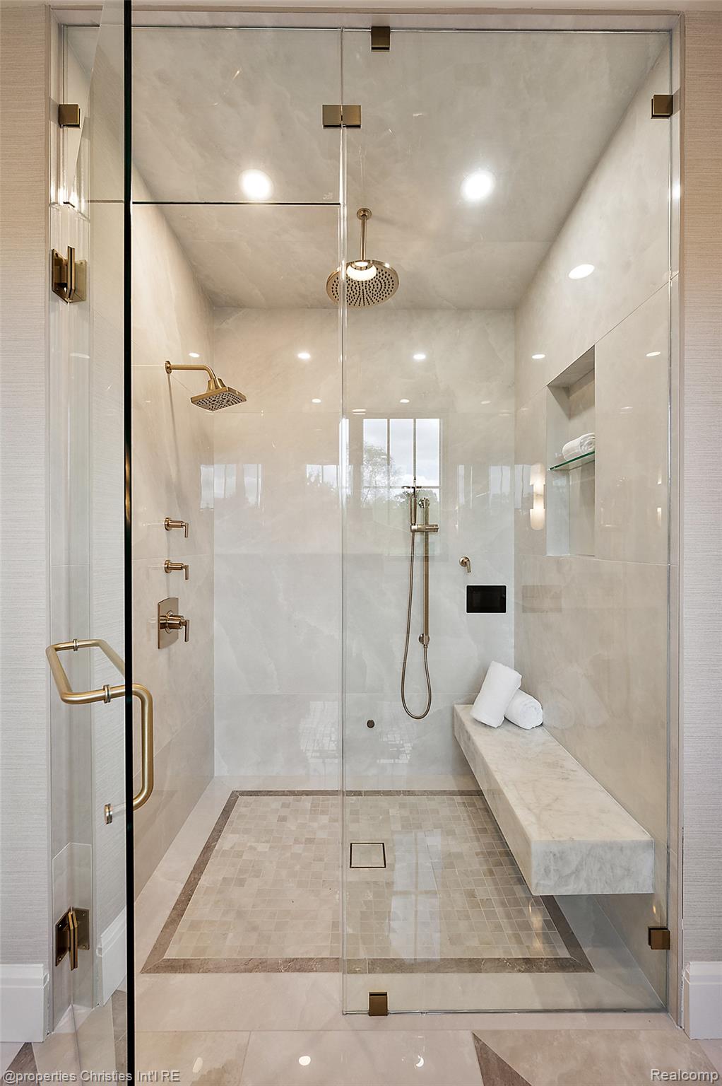 Walk-in shower with pale stone finishes, brass fixtures, and a long built-in bench.