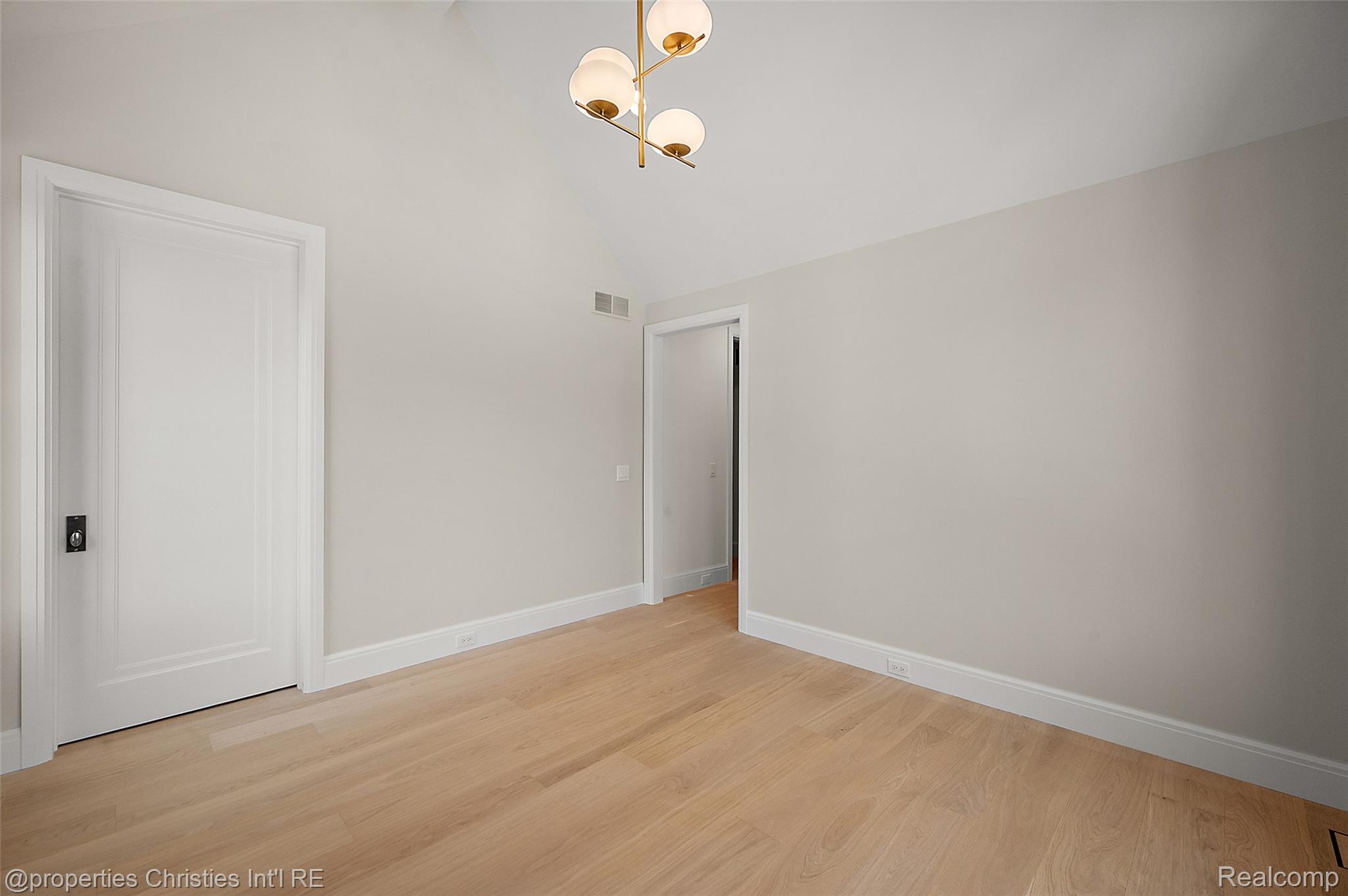 Unfurnished room with light wood floors, pale walls, and a brass pendant light.