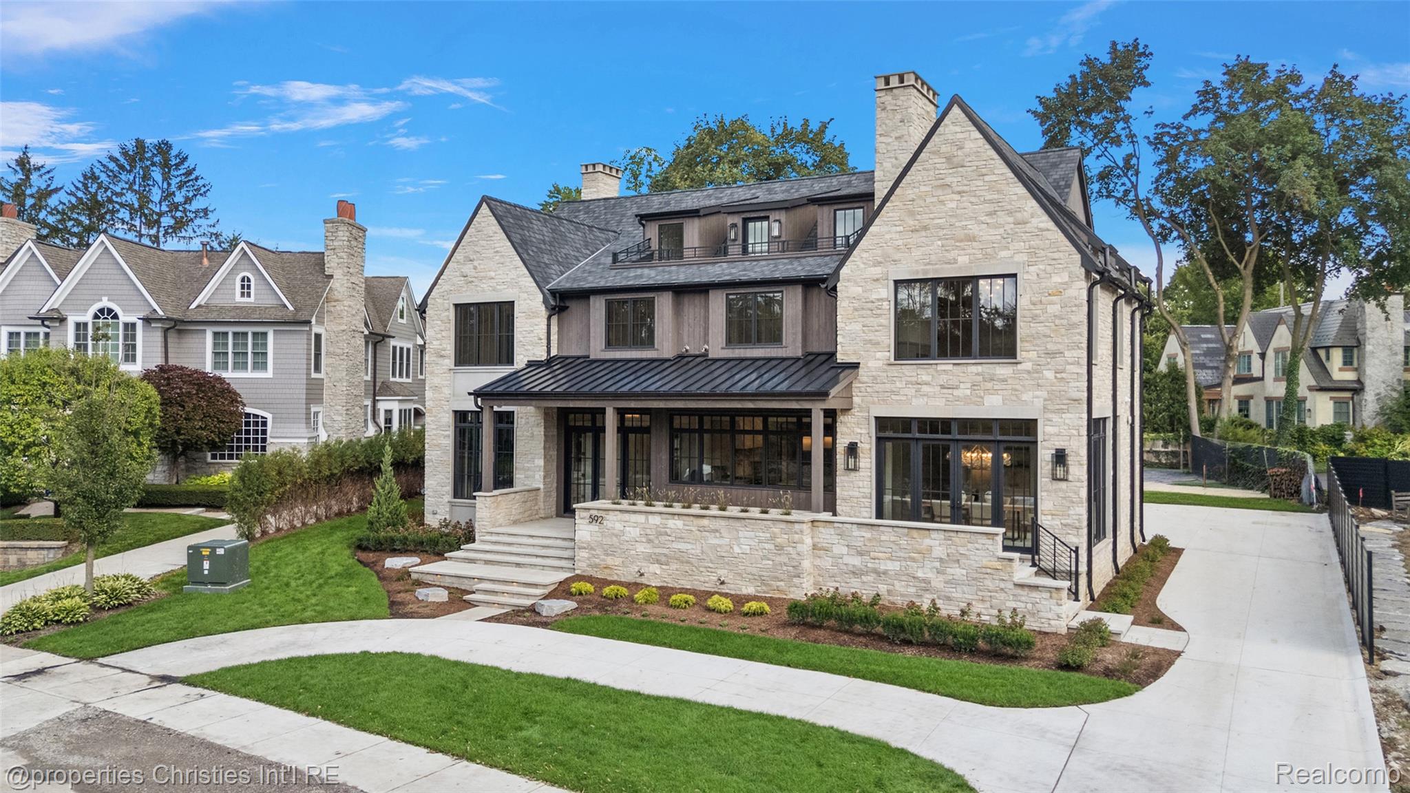 Stone two-story home with steep gabled roof, covered porch, and landscaped lawn.