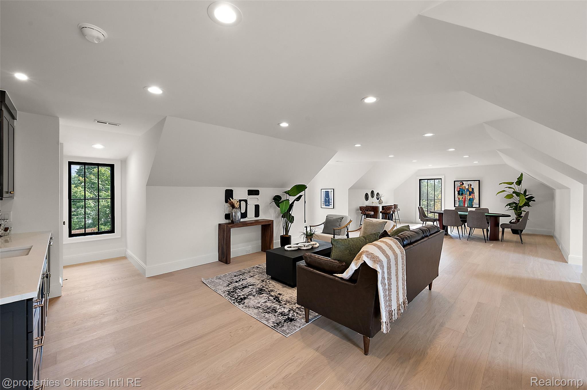 Open-plan living and dining area with a vaulted ceiling, brown sofa, and tall black-framed windows.