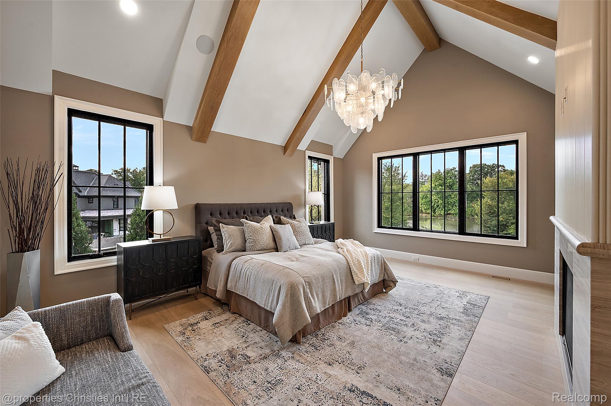 Staged bedroom with vaulted wood-beamed ceiling, crystal chandelier, and windows overlooking water.