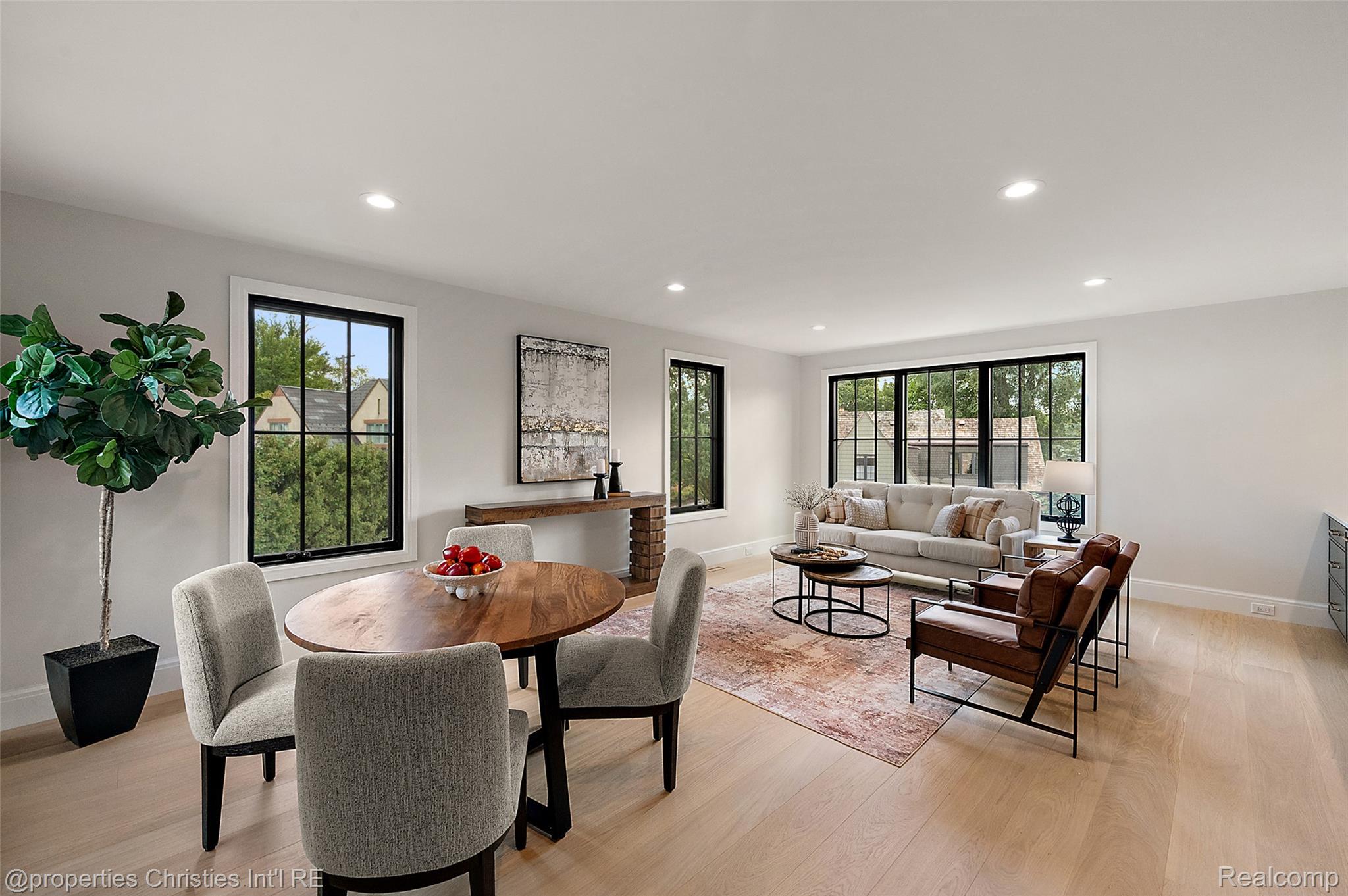 Open-plan living and dining room with black-framed windows, pale wood floors, and a round dining table.