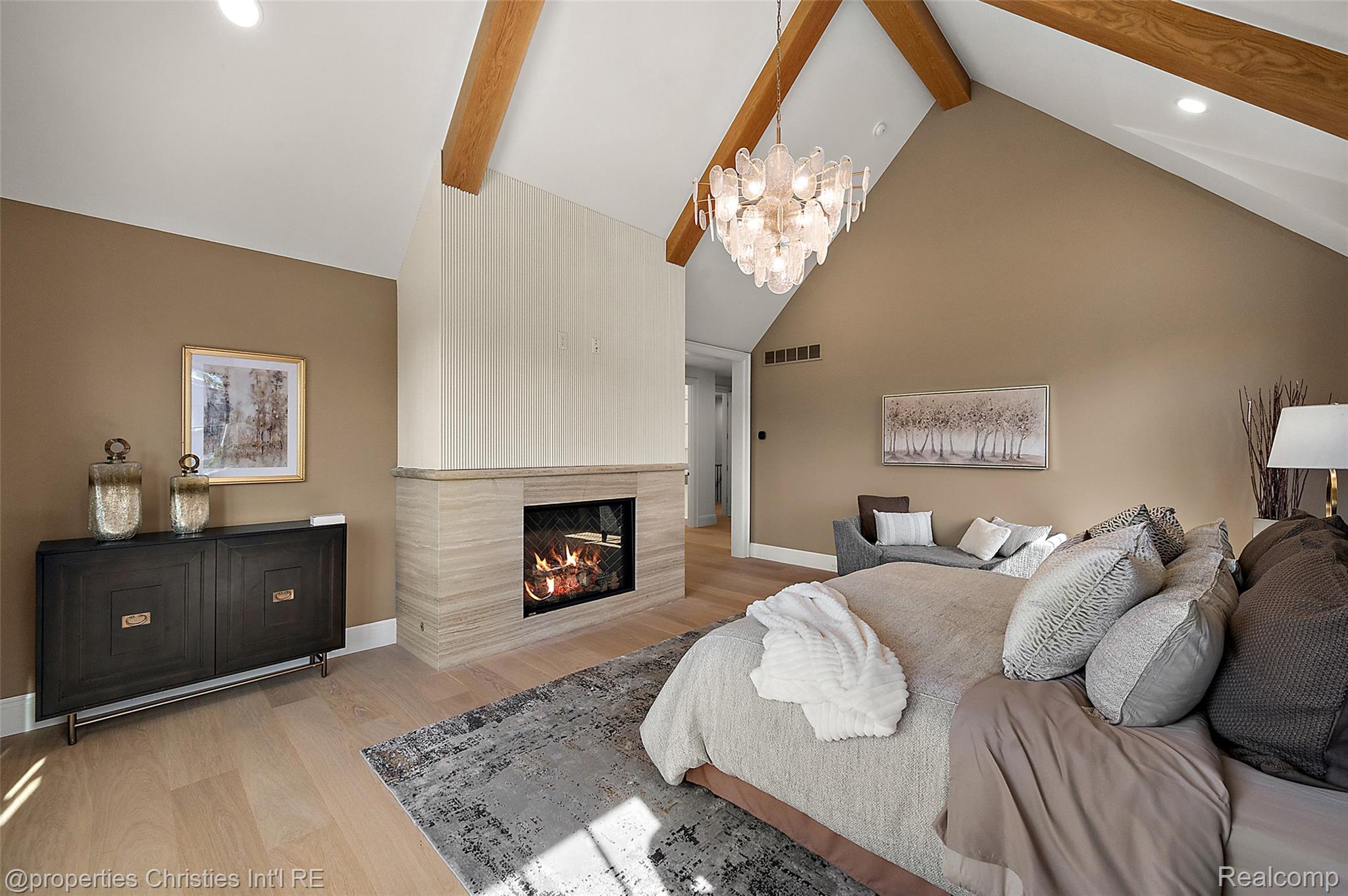 Living room with vaulted wood-beamed ceiling, chandelier, and a lit fireplace.